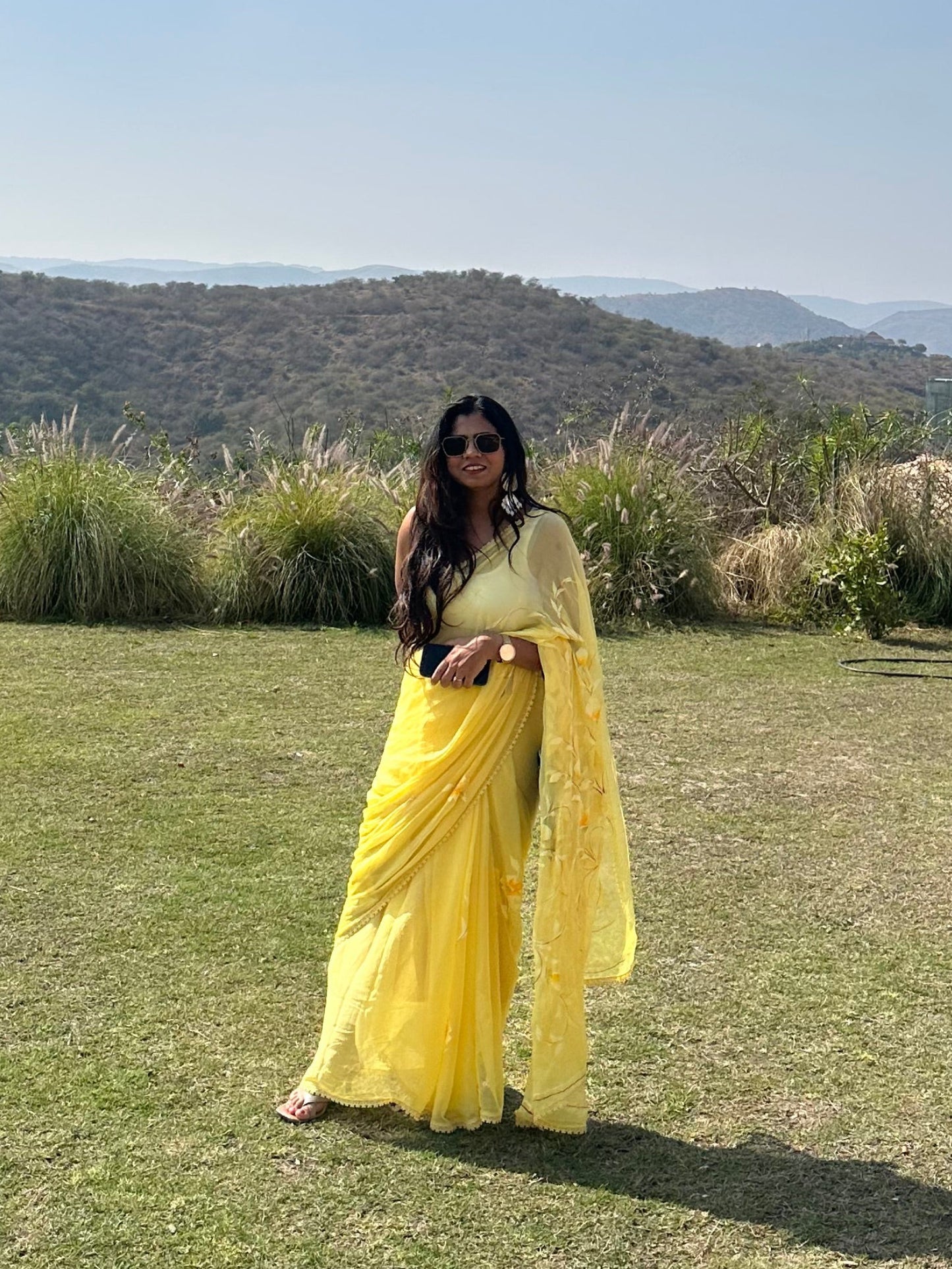Person in a yellow dress standing on a grassy field with mountains in the background