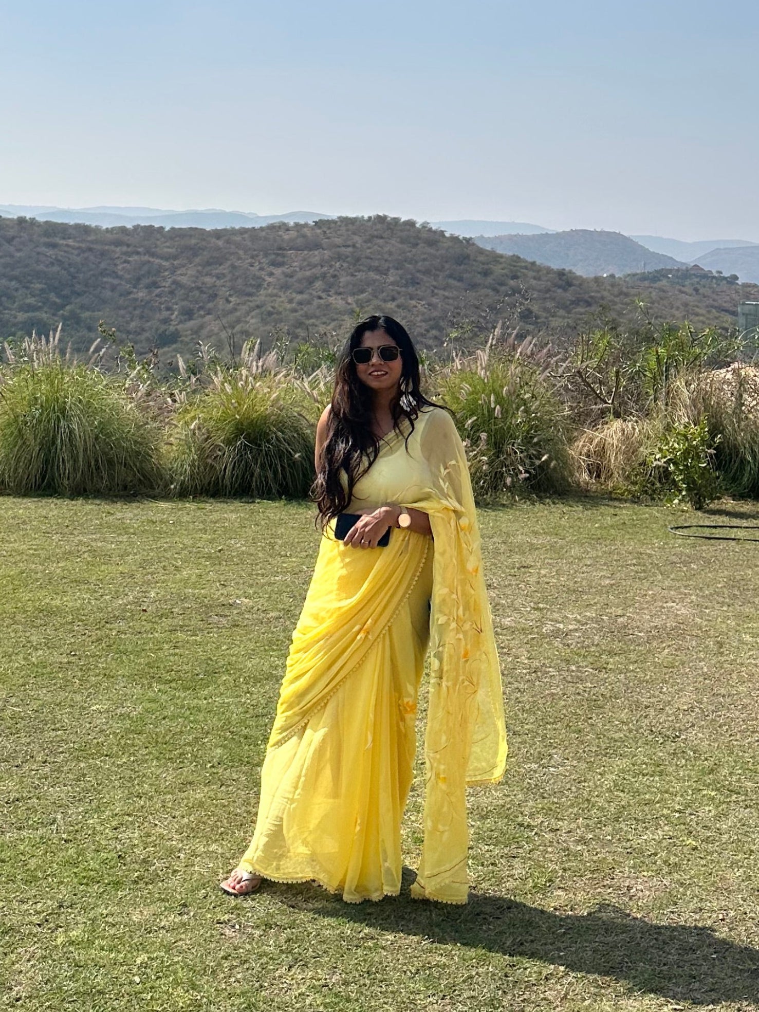 Person in a yellow dress standing on a grassy field with mountains in the background
